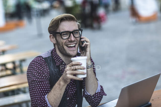 Young businessman chatting on smartphone at sidewalk cafe — Stock Photo