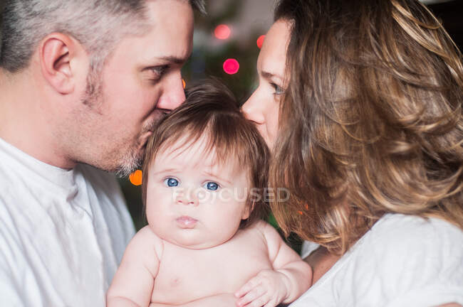 Madre y padre cara a cara sosteniendo a la niña, besándose en la cabeza - foto de stock