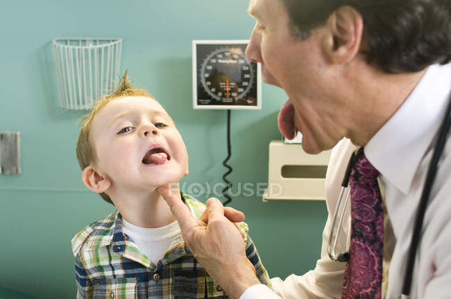 Médico varón mirando la lengua de un chico joven - foto de stock
