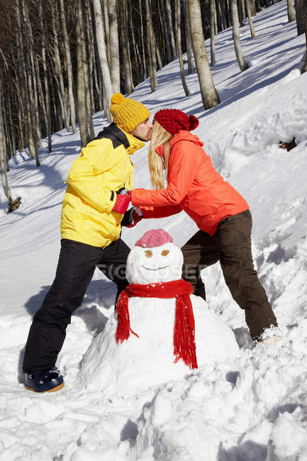 Couple kissing by snowman — Stock Photo