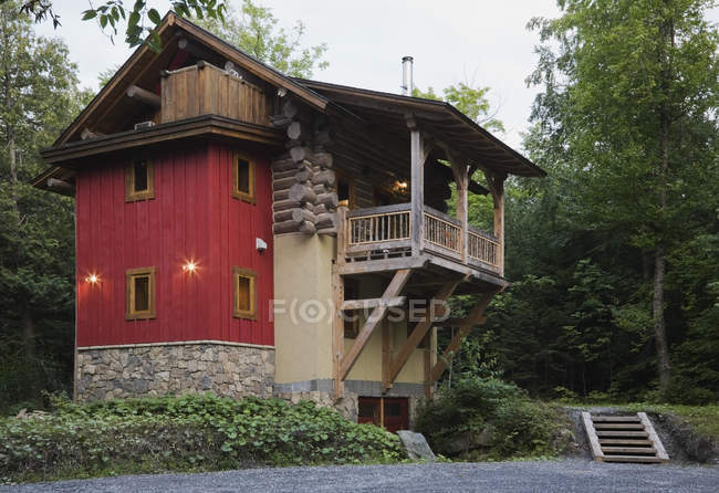 Cottage style log home with stone, red vertical wood siding and timber wood balcony at dusk in summer — Stock Photo
