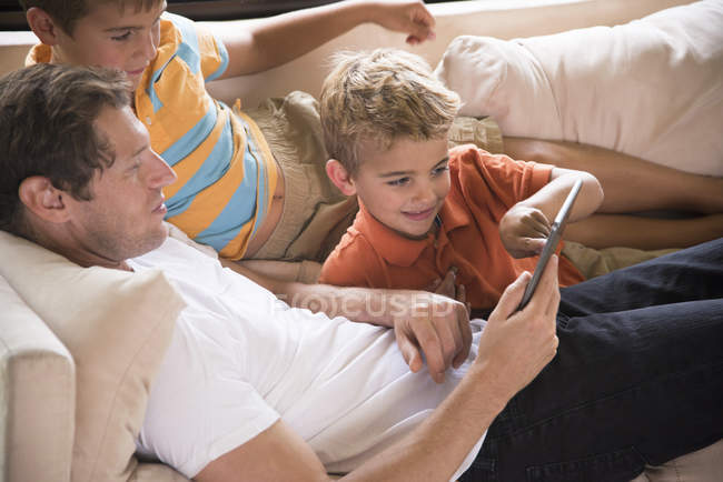 Человек и два сына указывают на цифровой планшет на диване — стоковое фото