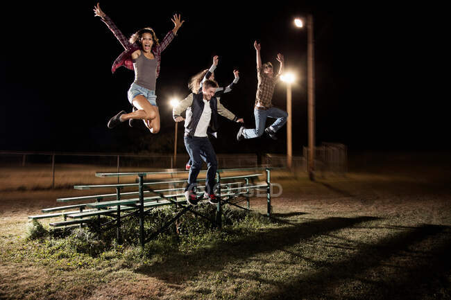 Cuatro amigos saltando sobre gradas por la noche - foto de stock