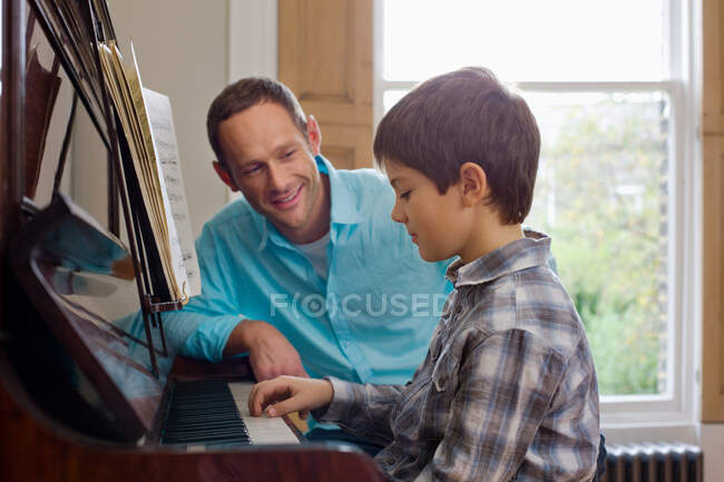 Padre enseñando a hijo a tocar el piano - foto de stock