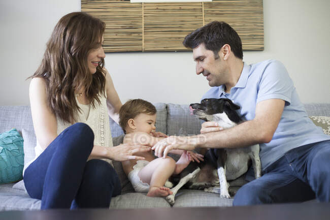 Famille avec bébé garçon assis sur le canapé jouant avec le chien — Photo de stock