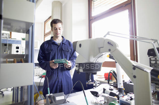Homme électricien regardant vers le bas à la carte de circuit dans l'atelier — Photo de stock