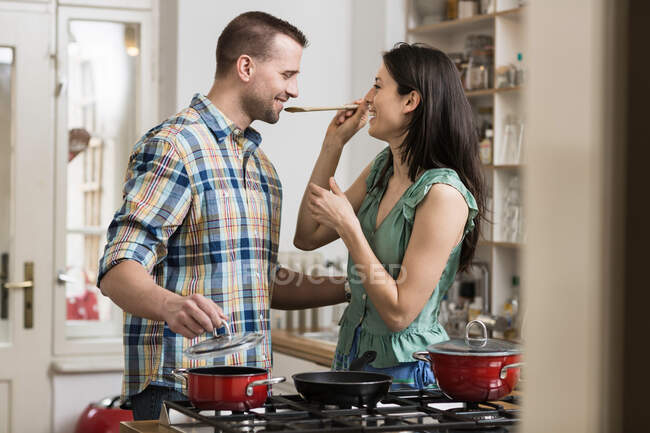 Средняя взрослая пара готовит ужин, дегустирует — стоковое фото