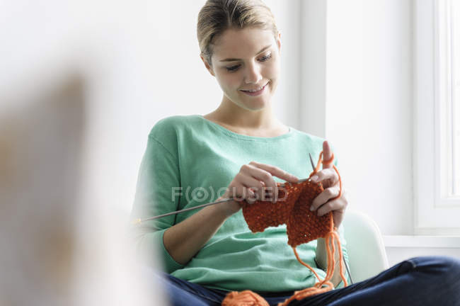 Jovem mulher sentada no assento da janela e tricô — Fotografia de Stock
