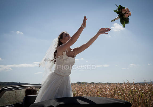 Newlywed bride tossing bouquet from car in field — Stock Photo
