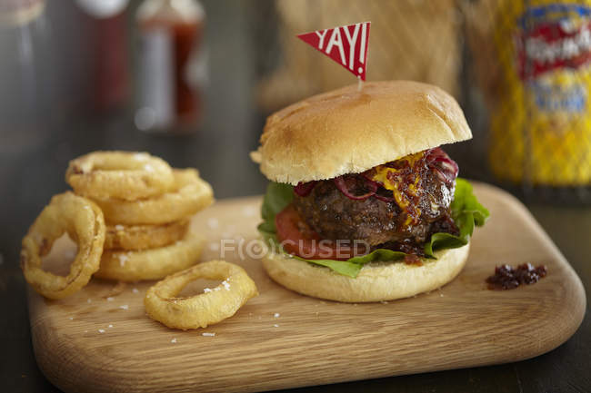 Burger and onion rings on wooden board — Stock Photo