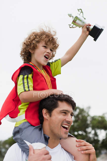 Тренер носит ребенка с трофеем — стоковое фото
