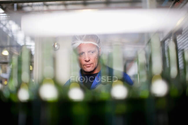 Trabalhador examinando garrafas na fábrica — Fotografia de Stock