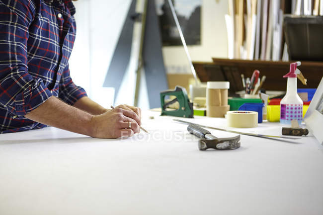 Homme adulte moyen écrivant la mesure sur l'établi dans l'atelier d'encadreurs de photo — Photo de stock