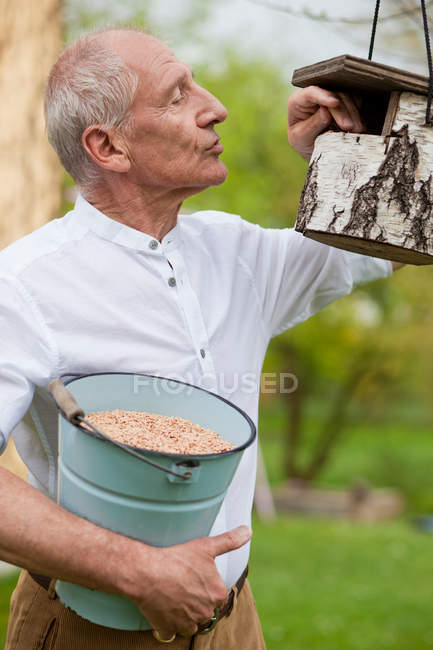Vieil homme remplissant une cabane à oiseaux — Photo de stock