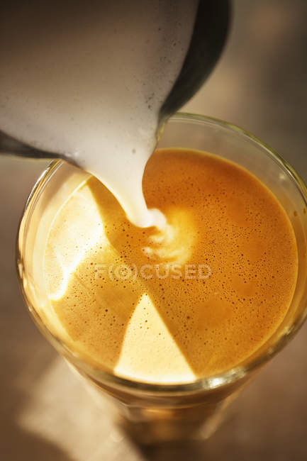 Close up of frothed milk pouring into coffee glass — Stock Photo