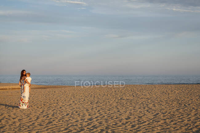 Mãe andando ao longo da praia, carregando criança — Fotografia de Stock
