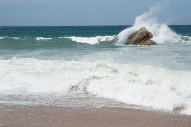 Onda colidindo contra a rocha no oceano sob céu limpo — Fotografia de Stock