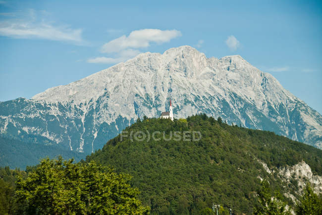 Iglesia en la colina frente a las montañas - foto de stock