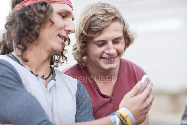 Dos amigos varones adultos jóvenes mirando el teléfono inteligente - foto de stock