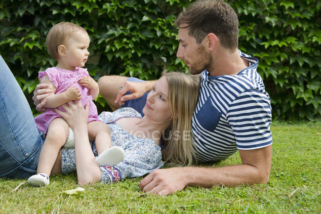 Mittleres erwachsenes Paar mit kleiner Tochter auf Rasen im Garten liegend — Stockfoto