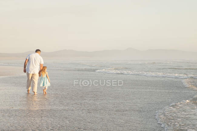 Отец и дочь держатся за руки и гребут в океане — стоковое фото
