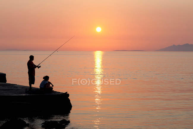 Couple fishing off pier at sunset, selective focus — Stock Photo