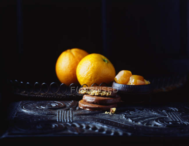 Galletas y naranjas con sabor a naranja recubiertas de chocolate en la mesa vintage - foto de stock