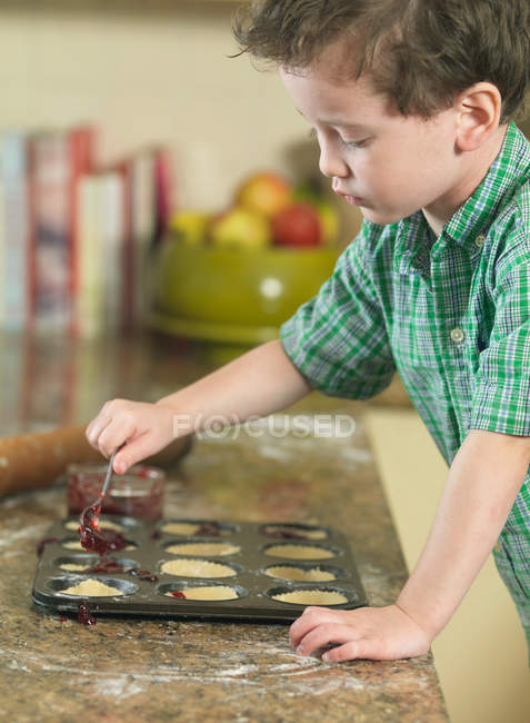 Garçon cuillère pâte dans la casserole dans la cuisine — Photo de stock