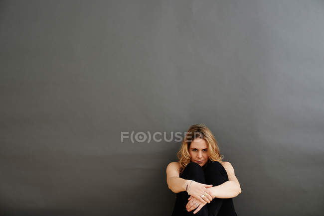 Взрослая женщина сидит, обнимая колени к груди — стоковое фото