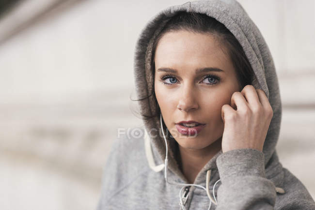 Female runner wearing grey hoody listening to music on earphones — Stock Photo