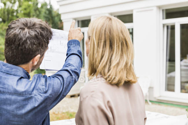 Rear view of architect discussing blueprints for house exterior with homeowner pointing — Stock Photo