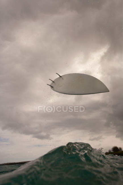 Surfboard in air above surf wave with cloudy sky — Stock Photo