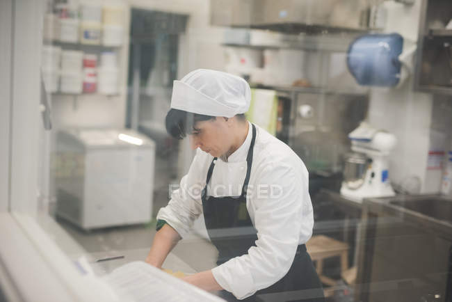 Женщина-пекарь катит тесто на кухне — стоковое фото