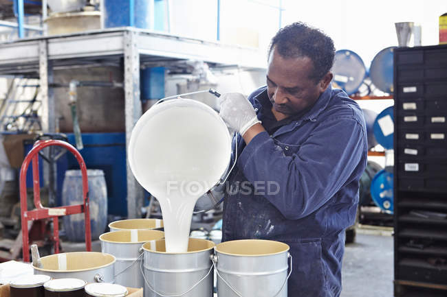 Trabajador vertiendo pintura en latas - foto de stock