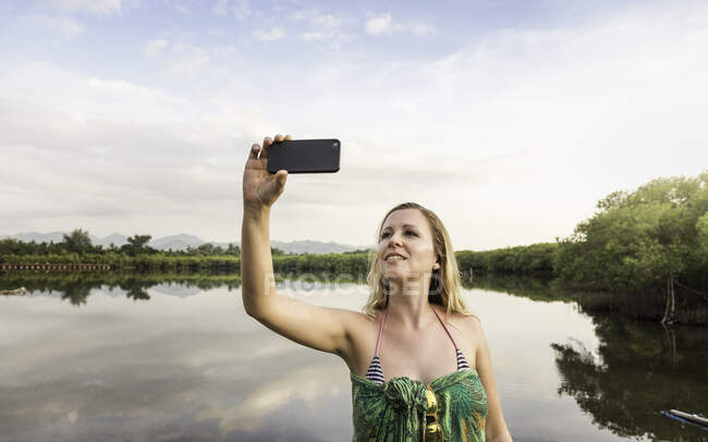 Mujer joven tomando selfie smartphone en frente del lago, Gili Meno, Lombok, Indonesia - foto de stock