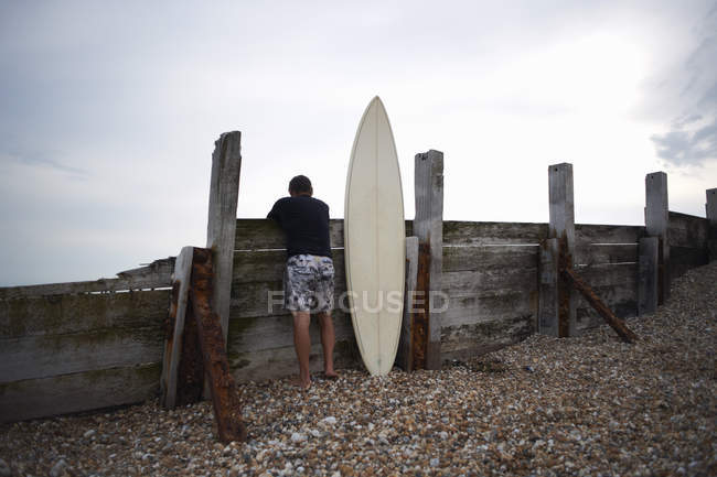 Surfer leaning against wooden fence with surfboard — Stock Photo