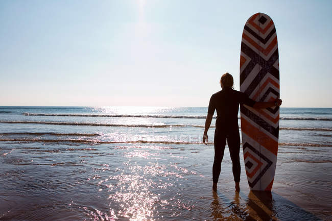 Чоловік стоїть на пляжі з дошкою для серфінгу — стокове фото