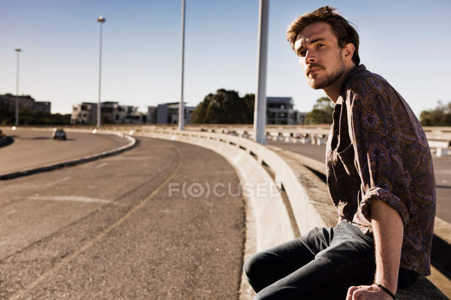 Joven hombre esperando un paseo al lado de una carretera - foto de stock