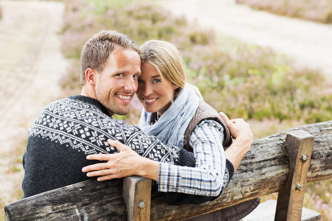 Casal adulto médio no banco de madeira olhando para a câmera — Fotografia de Stock