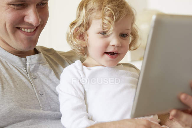 Женщина-ребенок сидит на колене отца с помощью цифрового планшета — стоковое фото