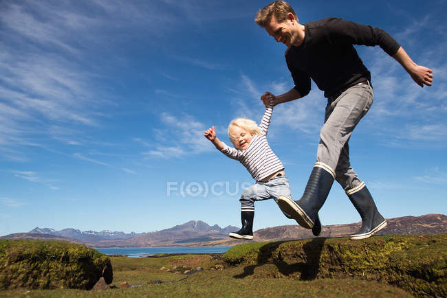 Padre e hijo tomados de la mano corriendo, Isla de Skye, Hébridas, Escocia - foto de stock