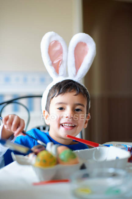 Хлопчик у вухах кролика малює великодні яйця — стокове фото