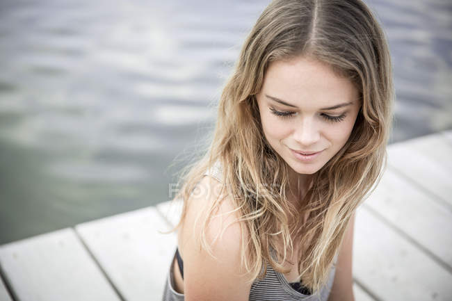 Giovane donna seduta sul molo, distogliendo lo sguardo — Foto stock