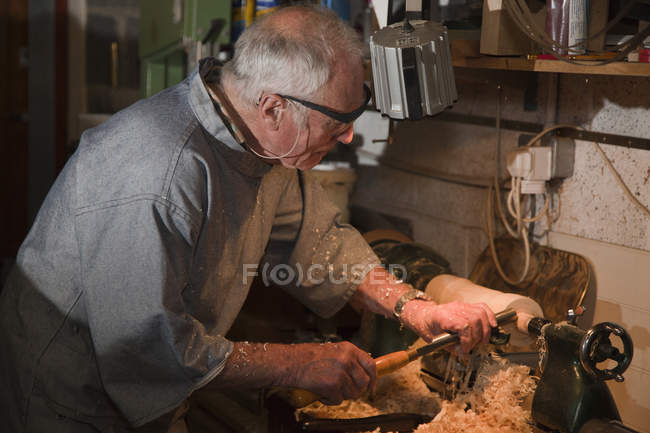 Старший чоловік формує шматок деревини столярними інструментами — стокове фото