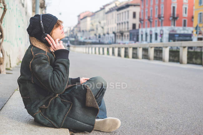 Man listening to music through headphones on kerb, Milan, Italy — Stock Photo