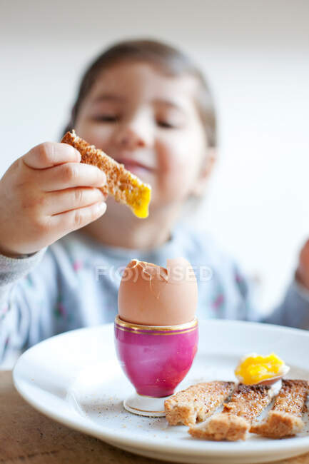 Дівчина занурює тости в яйце під час сніданку — стокове фото