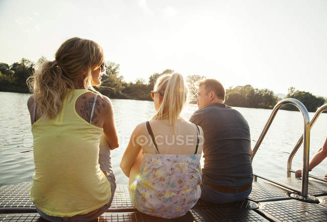 Tres amigos adultos jóvenes mirando desde el muelle de la orilla del río - foto de stock