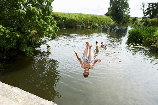 Adolescente somersaulting niño en rural lago - foto de stock