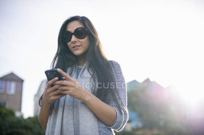 Jeune femme portant des lunettes de soleil avec smartphone — Photo de stock