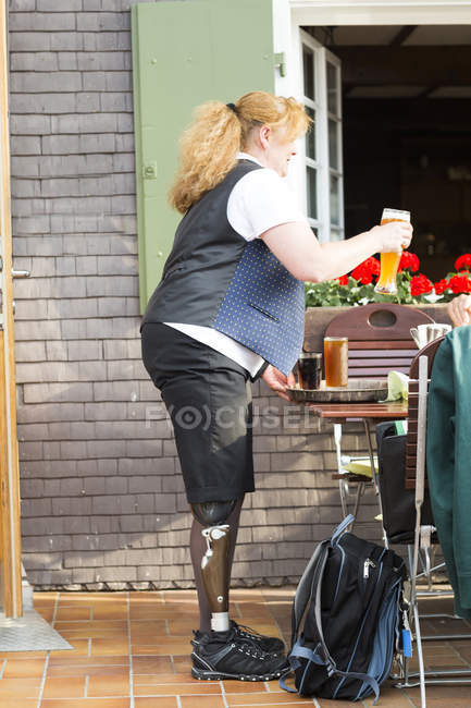 Femme adulte moyenne avec jambe prothétique, apportant des boissons au restaurant — Photo de stock
